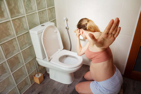 Pregnant woman with nausea by the toilet in bathの写真素材