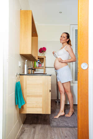 Pregnant woman stand in the bathroom near mirrorの写真素材