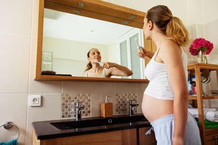 Pregnant woman brush teeth standing at bathroomの写真素材
