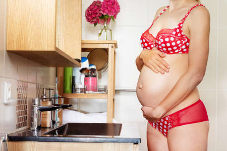 Pregnant woman in red lingerie hold big bellyの写真素材