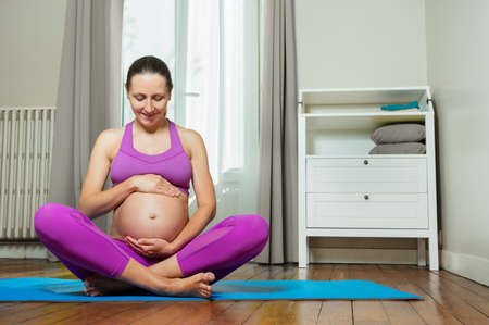 Pregnant in sport clothes hold belly on yoga matの写真素材