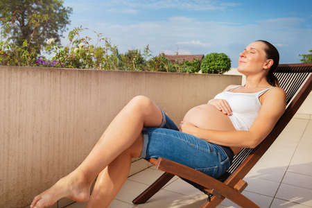 Pregnant woman rest in deck chair on the balconyの写真素材
