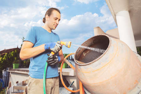 Young man stand cleaning cement mixer at home construction worksの写真素材