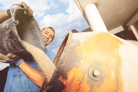 Close-up: a man pour out bucket of sand to cement mixerの写真素材