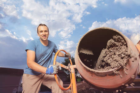 Happy guy pour concrete out of cement mixer at DIY home workの写真素材