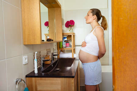 Pregnant woman in bathroom by mirror admire bellyの写真素材
