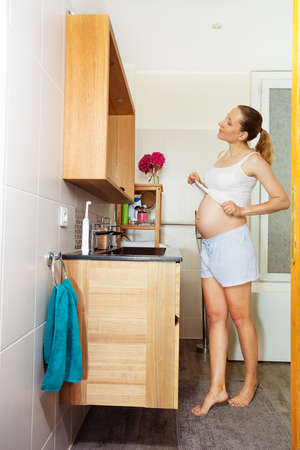 Pregnant woman in bath admire belly lift shirtの写真素材