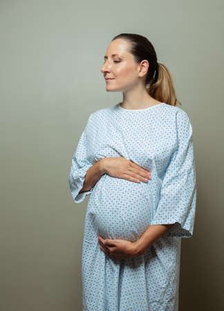 Pregnant woman in hospital robe hold big bellyの写真素材