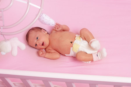 Newborn baby girl lay in the pink crib view from aboveの写真素材
