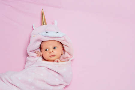 Newborn baby girl laying wrapped in unicorn pink blanketの写真素材