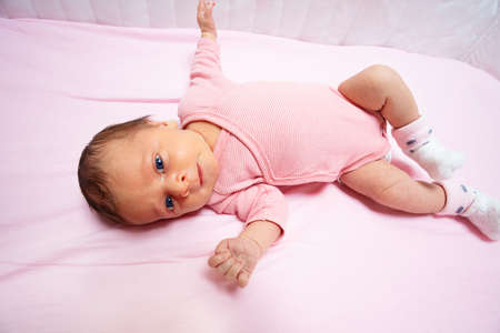 Little newborn baby girl lay in the pink cribの写真素材