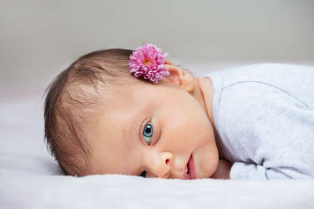 Newborn baby girl with flower lay on belly in the bedの写真素材
