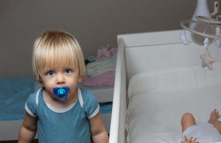 Little blond boy stand near the crib of newborn baby
