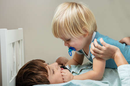 Little blond boy and his brother play in the bedの写真素材