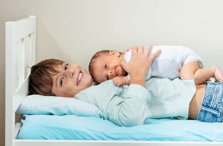 Laughing smiling boy lay in the bed hugging newborn sisterの写真素材
