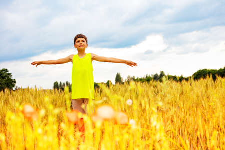 Boy stand in the wheat field with lifted up handsの写真素材