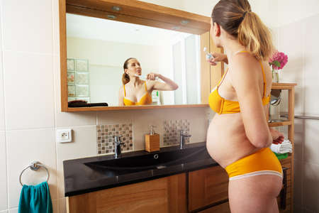 Pregnant woman in lingerie brush teeth at bathroomの写真素材