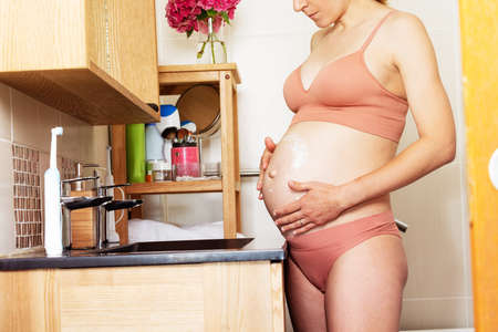 Pregnant woman apply cream on the belly, close-upの写真素材