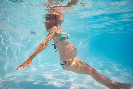 Pregnant woman exercise in outdoor pool underwaterの写真素材