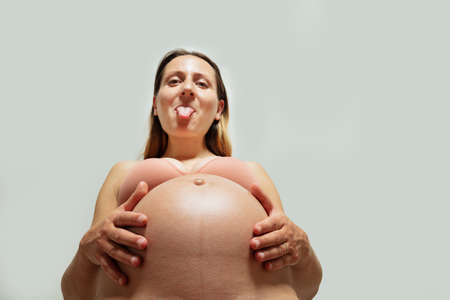 Playful pregnant woman stick out tongue hold belly look downの写真素材