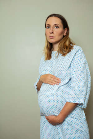 Pregnant woman with sad face hold big belly wear hospital robeの写真素材