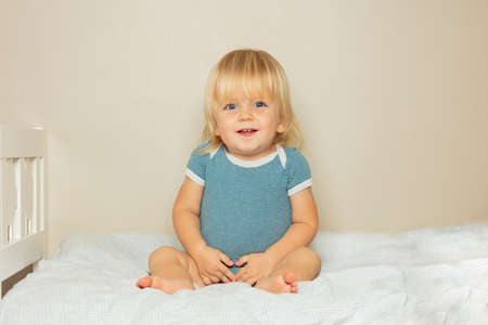 Smiling blond toddler boy sit on the bed in nurseryの写真素材