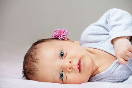Newborn baby infant with flower lay on belly in the bedの写真素材