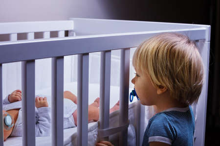 Toddler boy brother look in the crib of newborn sisterの写真素材