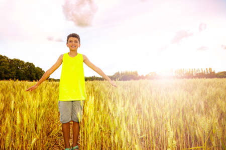 Young boy stand in the wheat field lifting up handsの写真素材