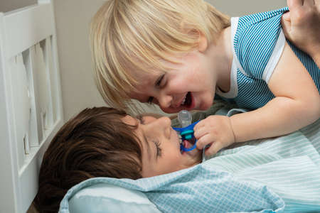 Little blond boy and his brother play in the bed with pacifierの写真素材
