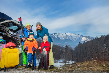 Mother at vacation stand holding ski by car arrived with 3 kidsの写真素材