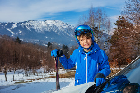 Happy young boy stand holding ski by car arrived at vacationの写真素材