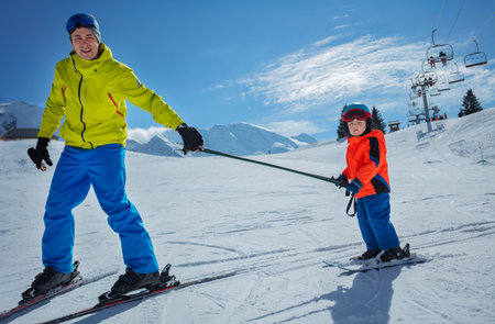 Dad go downhill teach child to ski connected by polesの写真素材