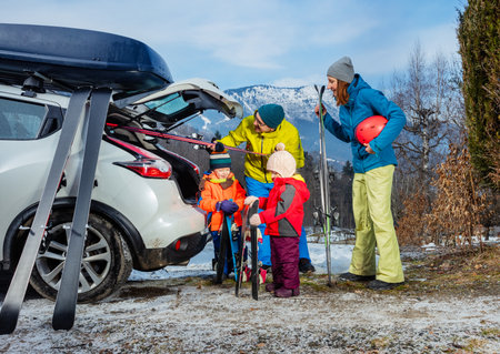 Family mom dad and two children unload ski from car by mountainの写真素材