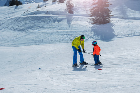 Dad glide backwards teaching little child to ski using polesの写真素材