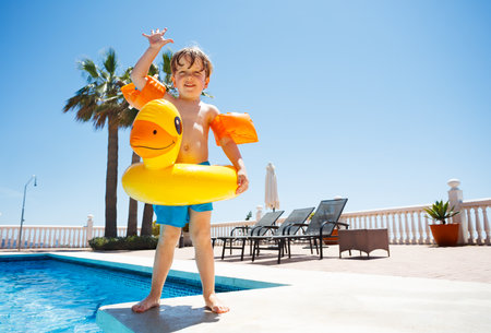 Cute boy waving hands standing on the edge of swimming poolの写真素材