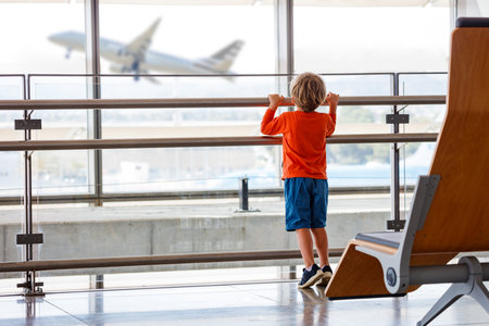 Young boy watches a plane take off from an airport windowの写真素材