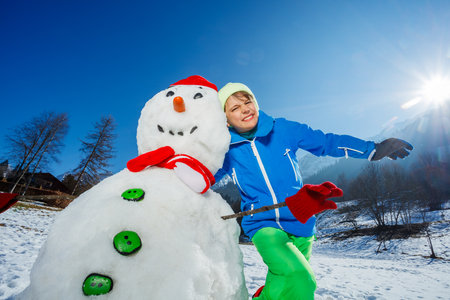 Child in winter outfit cuddles snowman over mountain rangeの写真素材