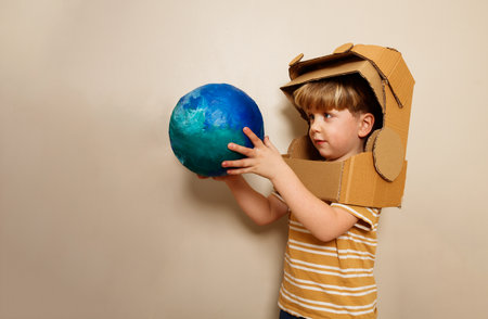 A child with cardboard astronaut helmet holds earth globeの写真素材