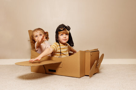 Kids sit in cardboard plane, wear hats and glasses pretend flyの写真素材