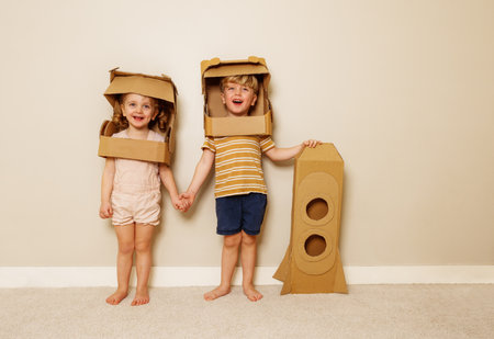 Boy, girl hold hands with cardboard astronaut helmets and rocketの写真素材