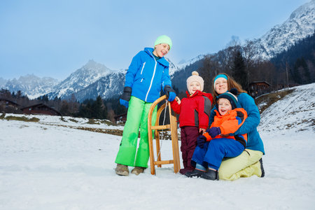 Mom and three children play outside on snow slope with sledgeの写真素材