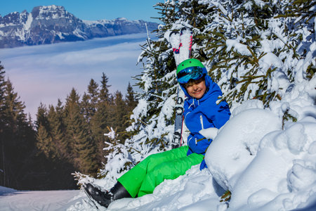 Boy with ski helmet and googles hold skies smile sit in snowの写真素材