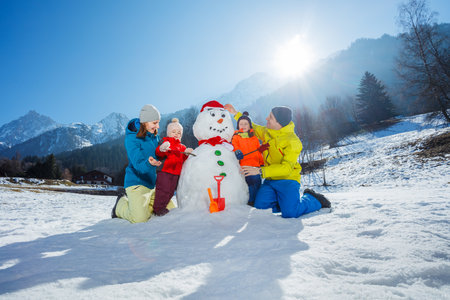 Mother, father, and their kids, collaborate to build a snowmanの写真素材