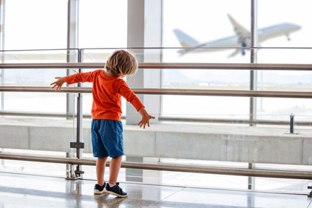 Young child watches a plane take off from an airport windowの写真素材