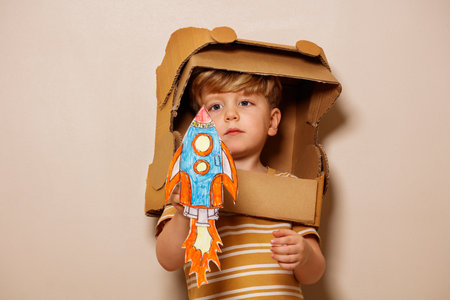 Child plays paper rocket, wears cardboard astronaut helmetの写真素材