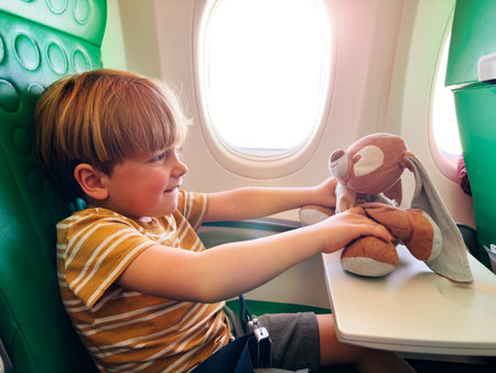 Cute boy cuddles toy, fly in the plane near windowの写真素材