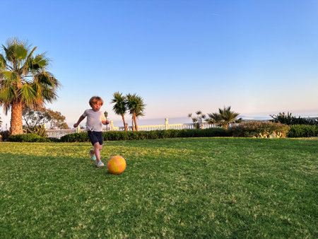 Little boy play football on lawn in sunset lightsの写真素材
