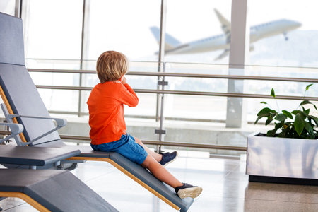 Young boy eagerly watches planes from airport chairの写真素材