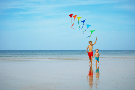 Boys run holding many colorful kites at the beach smilingの写真素材